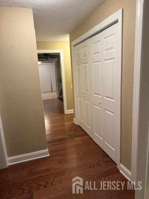 hallway with a textured ceiling and dark wood-type flooring