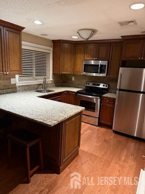 kitchen with light stone countertops, sink, kitchen peninsula, light hardwood / wood-style floors, and appliances with stainless steel finishes