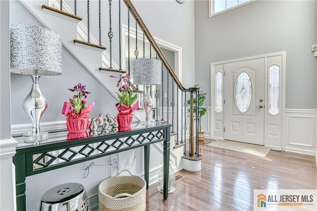 foyer with stairway, a wainscoted wall, a towering ceiling, a decorative wall, and wood-type flooring