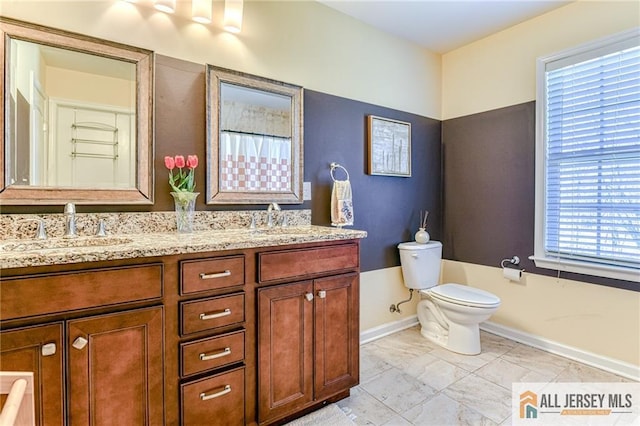 bathroom featuring a sink, baseboards, toilet, and double vanity