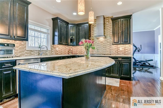 kitchen with a center island, wall chimney range hood, ornamental molding, wainscoting, and wood-type flooring