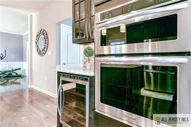 kitchen featuring wine cooler, crown molding, wood-type flooring, wainscoting, and double oven