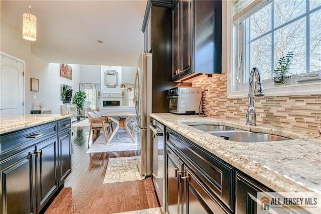 kitchen with light wood-style flooring, a sink, tasteful backsplash, freestanding refrigerator, and light stone countertops