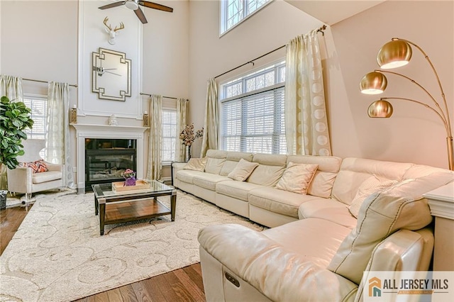 living area with a glass covered fireplace, dark wood-style floors, ceiling fan, and a towering ceiling