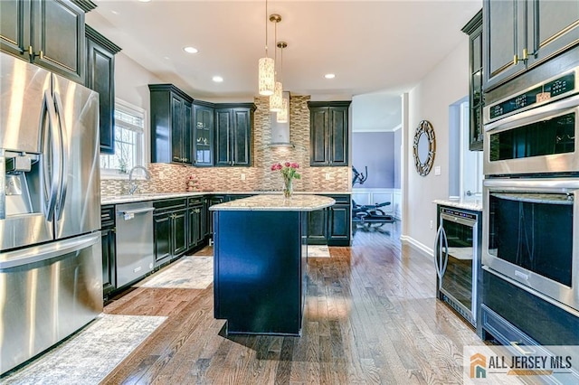 kitchen featuring backsplash, stainless steel appliances, wine cooler, wood-type flooring, and wall chimney exhaust hood