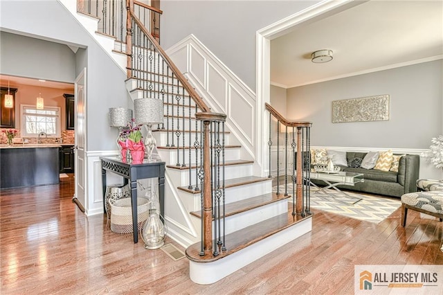 staircase with a wainscoted wall, wood finished floors, a towering ceiling, and ornamental molding