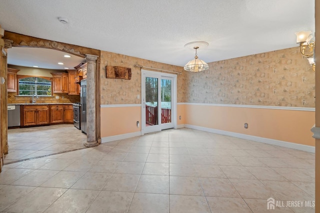 unfurnished dining area featuring decorative columns, a textured ceiling, a sink, and wainscoting