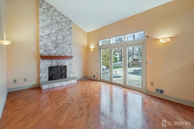 unfurnished living room featuring light wood-style floors, visible vents, high vaulted ceiling, and a stone fireplace