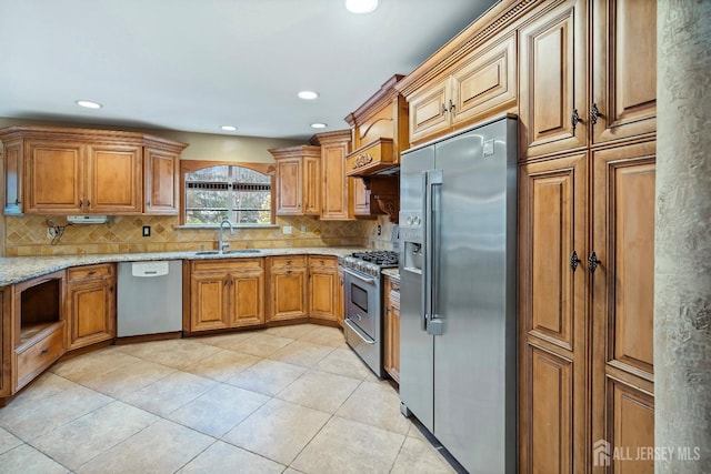 kitchen with premium appliances, light stone counters, brown cabinets, tasteful backsplash, and a sink