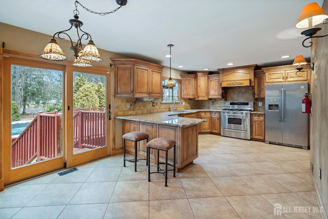 kitchen with appliances with stainless steel finishes, light stone counters, a kitchen breakfast bar, a peninsula, and pendant lighting