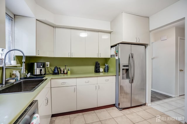 kitchen with appliances with stainless steel finishes, a sink, light countertops, white cabinetry, and light tile patterned floors