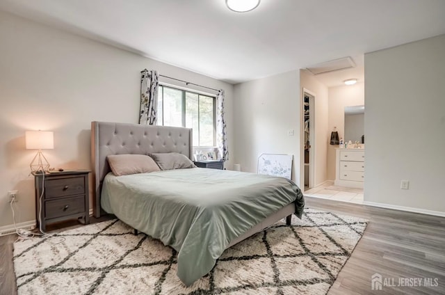 bedroom with wood finished floors, attic access, baseboards, and ensuite bath