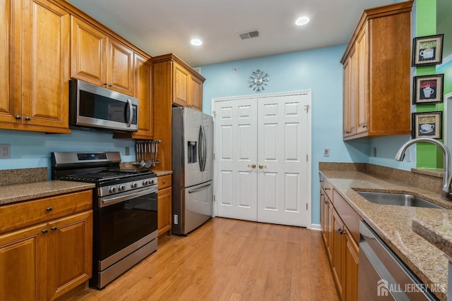 kitchen with light stone counters, appliances with stainless steel finishes, sink, and light hardwood / wood-style flooring