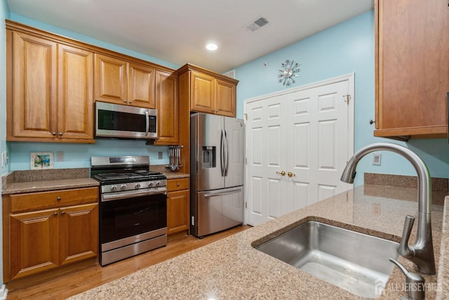 kitchen with light stone countertops, appliances with stainless steel finishes, sink, and light hardwood / wood-style floors