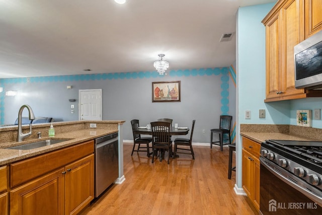 kitchen with sink, a chandelier, light wood-type flooring, appliances with stainless steel finishes, and light stone countertops