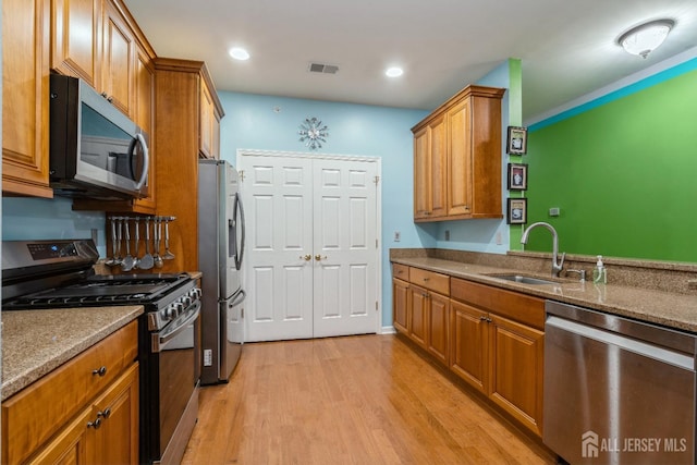 kitchen featuring stainless steel appliances, stone countertops, sink, and light hardwood / wood-style flooring