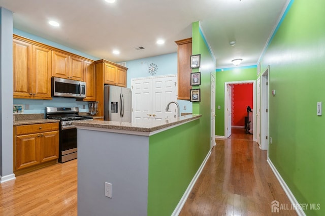 kitchen with appliances with stainless steel finishes, sink, crown molding, light stone countertops, and light hardwood / wood-style flooring