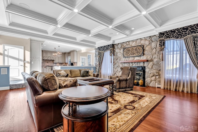 living room with a chandelier, ornamental molding, a stone fireplace, and wood finished floors