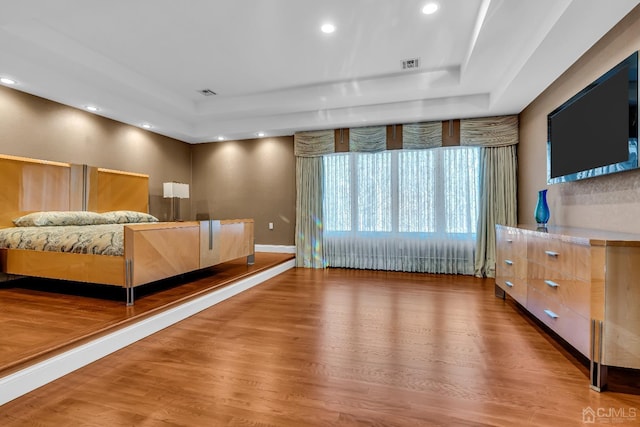 unfurnished bedroom with wood finished floors, a raised ceiling, and visible vents