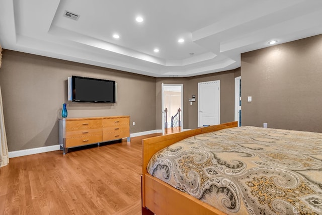 bedroom with light wood-style floors, baseboards, visible vents, and a tray ceiling