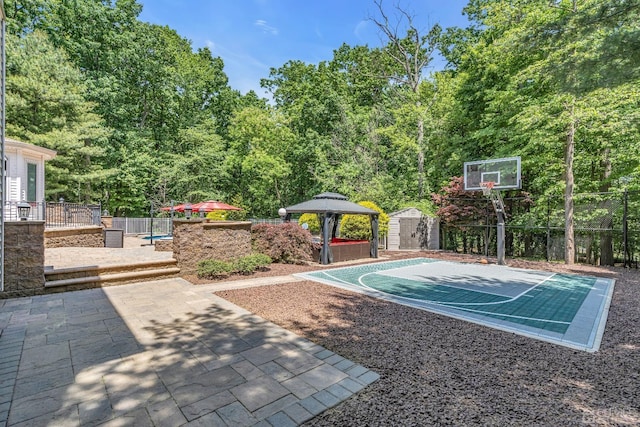 view of basketball court with basketball hoop, a storage unit, a gazebo, and fence