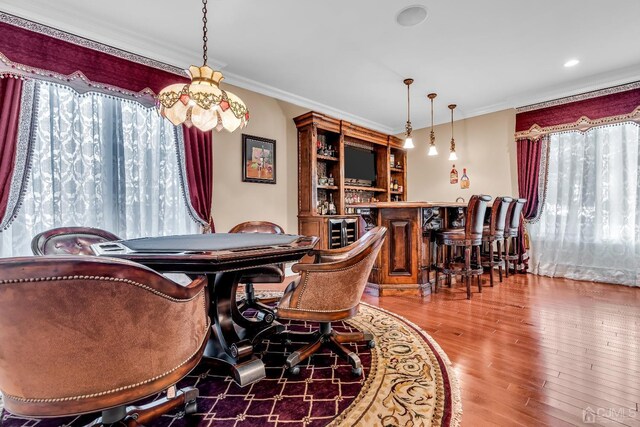 dining space featuring bar area, hardwood / wood-style flooring, and ornamental molding