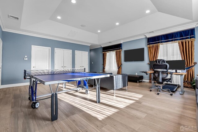 game room featuring a raised ceiling, light wood-type flooring, and ornamental molding