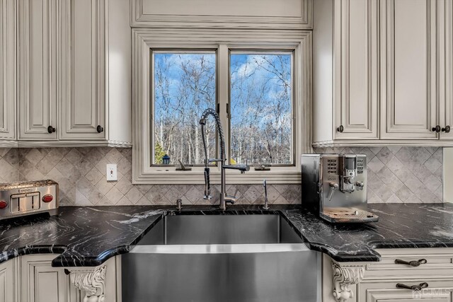 kitchen featuring backsplash, dark stone countertops, white cabinetry, and sink