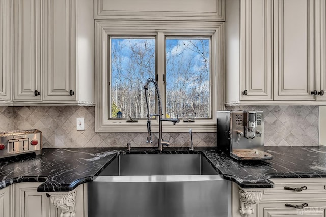 kitchen featuring tasteful backsplash, dark stone countertops, a sink, and a healthy amount of sunlight