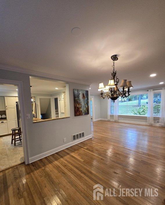 unfurnished dining area featuring a notable chandelier, wood-type flooring, and crown molding