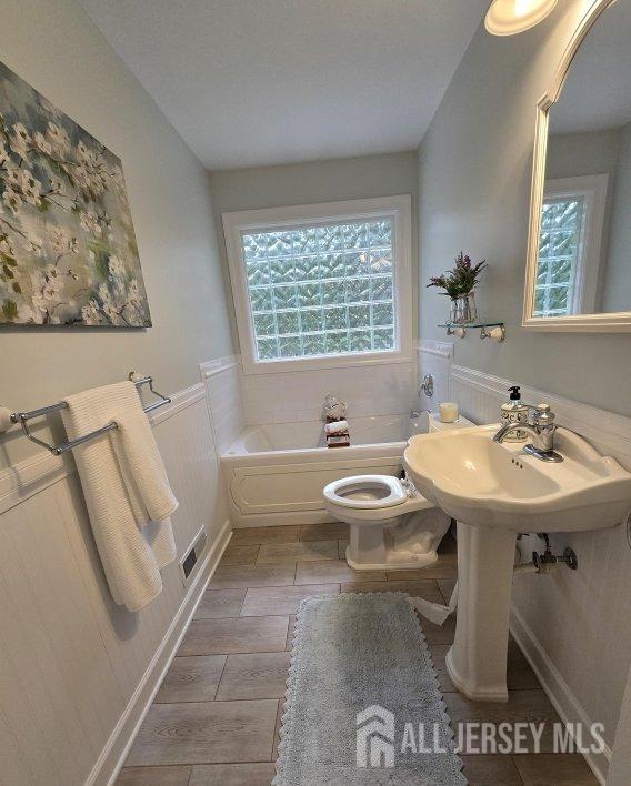 full bathroom with toilet, a bath, visible vents, and a wainscoted wall