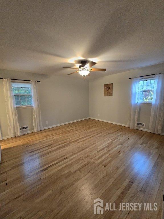 spare room with ceiling fan, visible vents, light wood finished floors, and a textured ceiling