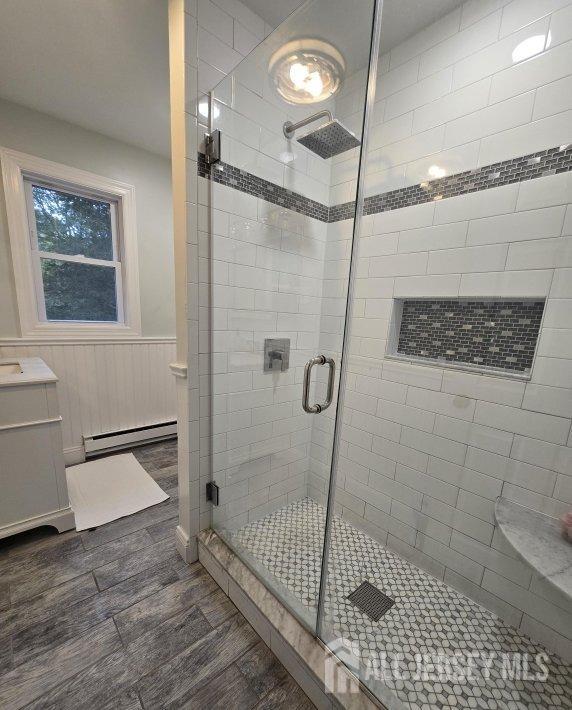 bathroom featuring vanity, a shower with shower door, and a baseboard heating unit