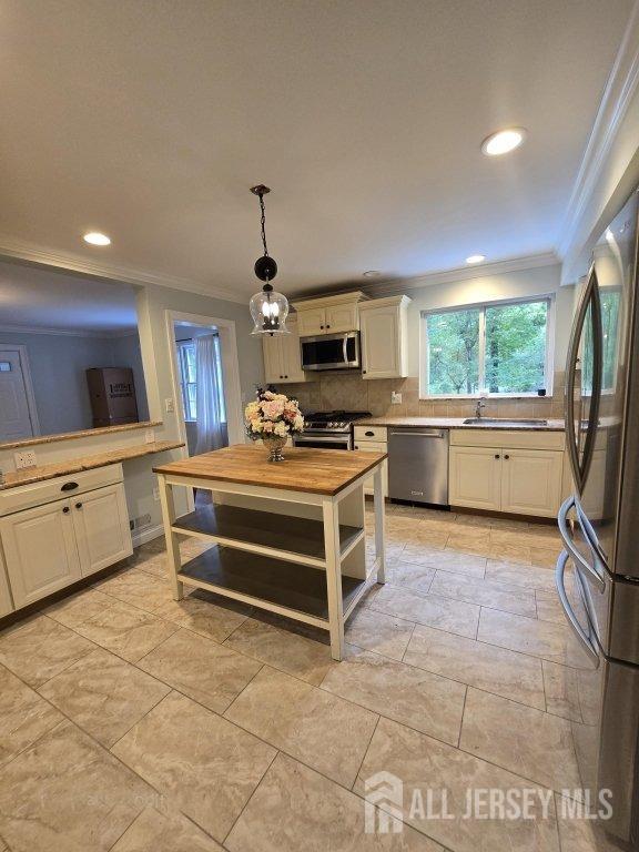 kitchen featuring white cabinetry, hanging light fixtures, wooden counters, appliances with stainless steel finishes, and ornamental molding