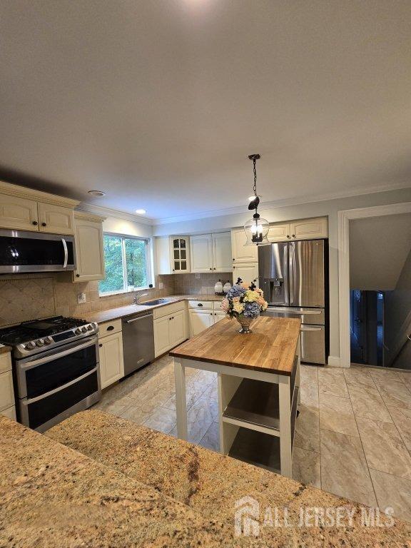 kitchen featuring wooden counters, sink, ornamental molding, decorative light fixtures, and stainless steel appliances