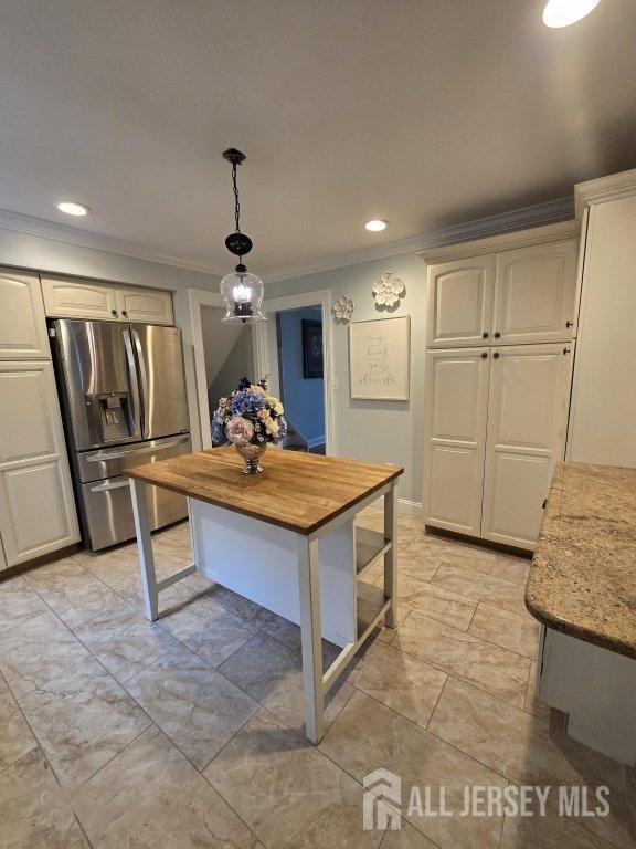 kitchen with stainless steel fridge, crown molding, pendant lighting, and light stone counters