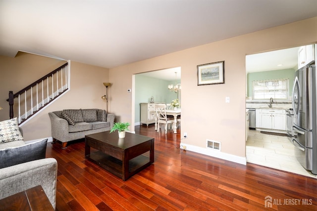 living room with visible vents, baseboards, stairs, wood finished floors, and a notable chandelier