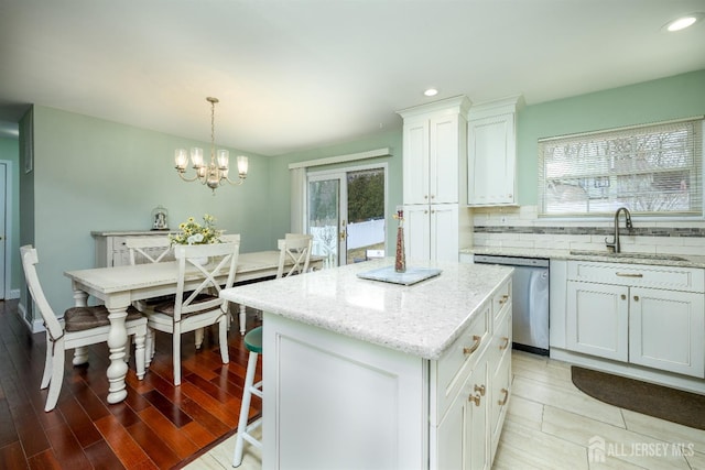 kitchen featuring a sink, tasteful backsplash, stainless steel dishwasher, a kitchen island, and a healthy amount of sunlight