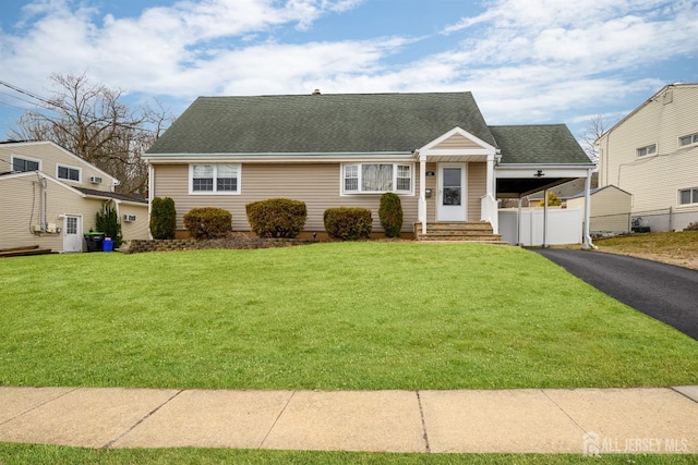 view of front of home with aphalt driveway, a shingled roof, a front yard, and fence