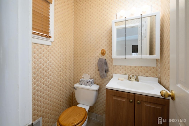 half bathroom featuring toilet, wallpapered walls, and vanity