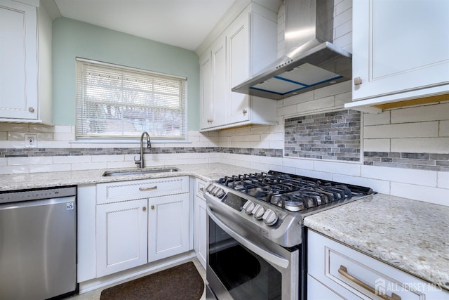 kitchen with a sink, appliances with stainless steel finishes, wall chimney exhaust hood, white cabinets, and decorative backsplash