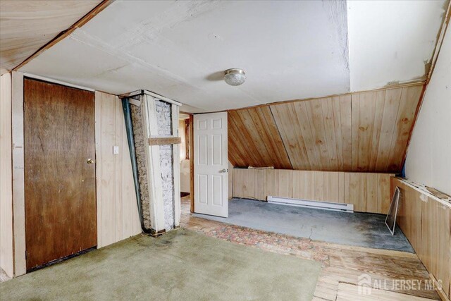 additional living space featuring wooden walls, a baseboard radiator, and vaulted ceiling