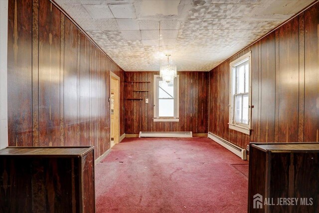 carpeted spare room with an inviting chandelier, wood walls, and a baseboard heating unit