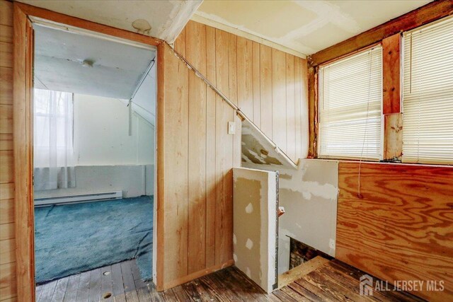 staircase featuring wooden walls, a baseboard radiator, and hardwood / wood-style floors