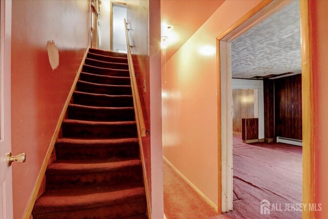 stairs featuring a baseboard heating unit, wood walls, and carpet