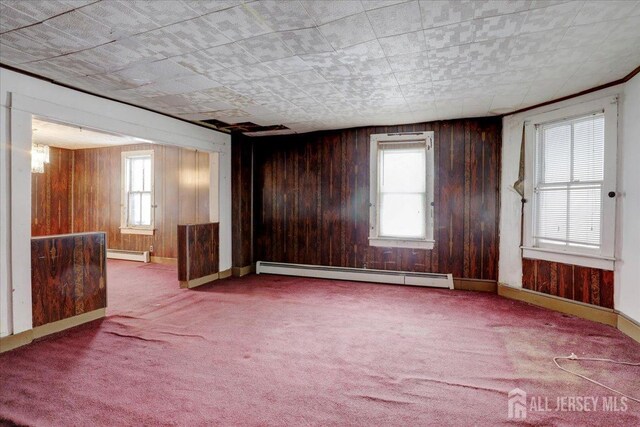 carpeted empty room with plenty of natural light, a baseboard radiator, and wooden walls