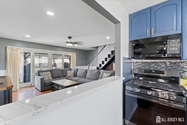 kitchen with black microwave, stainless steel gas range oven, blue cabinets, backsplash, and light stone countertops