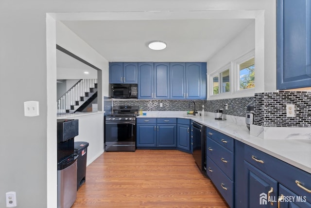 kitchen featuring tasteful backsplash, light wood-style flooring, blue cabinets, black appliances, and a sink