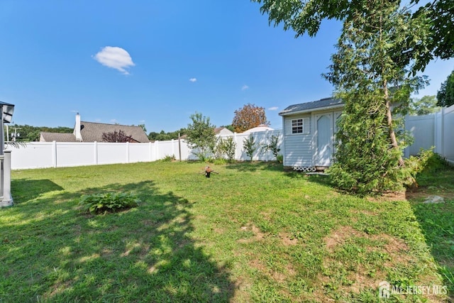 view of yard with a storage shed, a fenced backyard, and an outbuilding