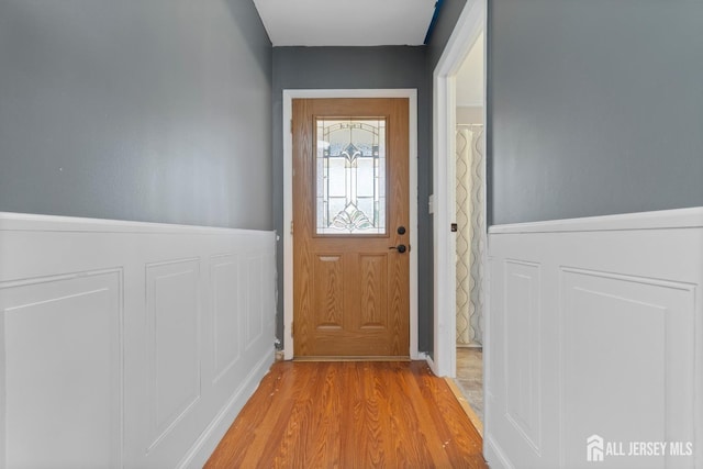 entryway featuring light wood finished floors, a decorative wall, and wainscoting